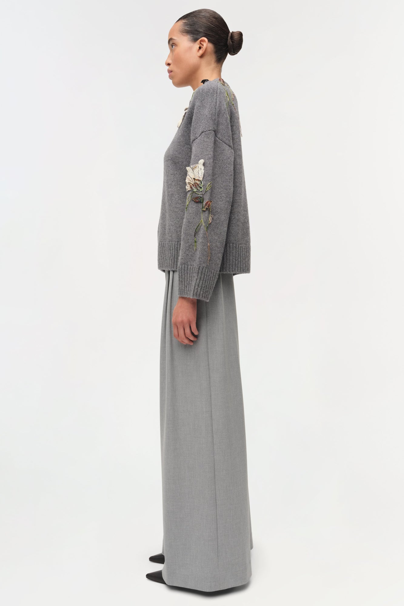 Gray knit sweater with floral embroidery on sleeve, worn with gray maxi skirt.