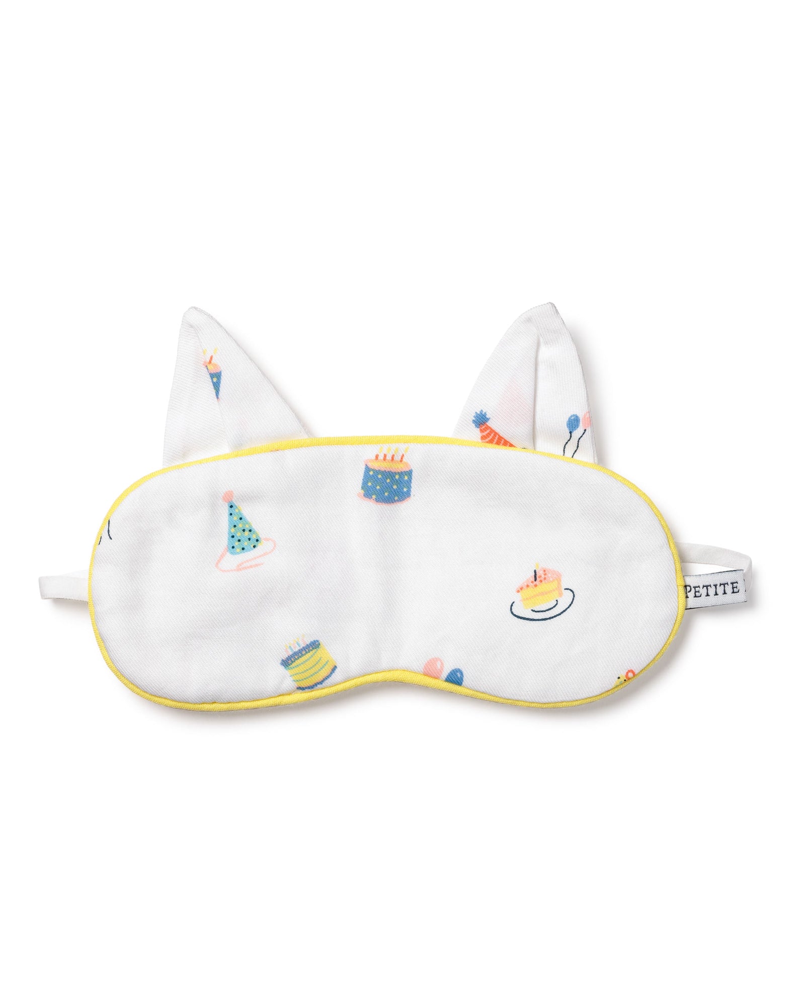 The Kids Twill Kitty Sleep Mask in Birthday Wishes by Petite Plume is a luxurious white eye mask with yellow trim, featuring colorful cake, party hat, and balloon illustrations. It includes two fabric ears, an elastic strap, and can be monogrammed for personalization.