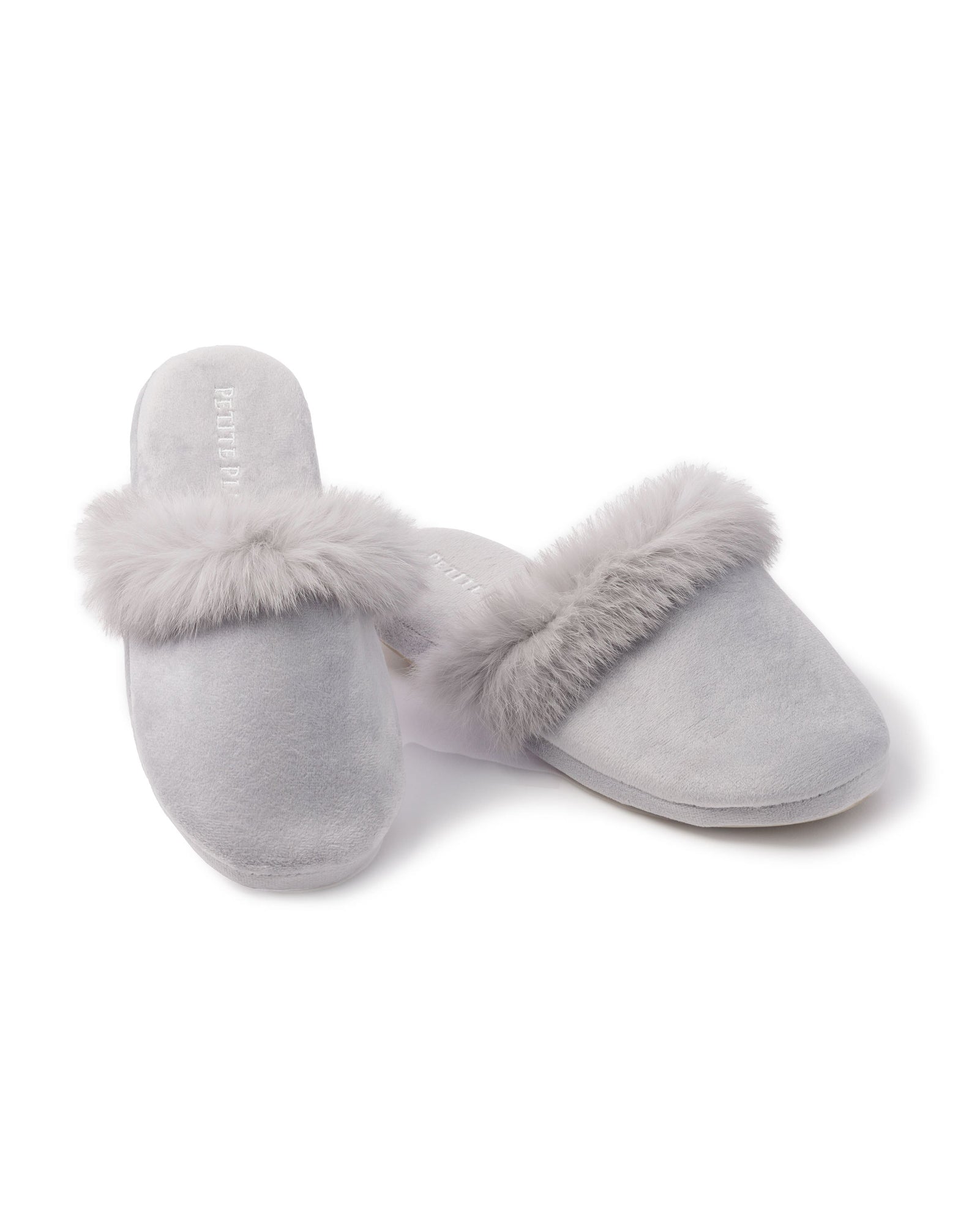 A pair of Womens Faux Fur Trim Slippers in light gray by Petite Plume, showcasing plush comfort with soft fur trim, is displayed on a white background. One slipper stands upright while the other rests elegantly on its side.