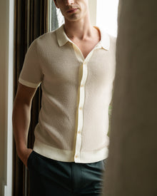 Man wearing a light-colored short-sleeve shirt and dark pants indoors.