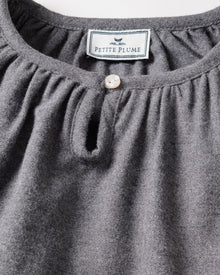 Close-up of a grey nightgown showcasing a round neckline and pearl-like button. Inside, the label reads Petite Plume with a bird graphic. Made from brushed cotton flannel, its texture highlights the softness and chemical-free comfort of the Girls Flannel Delphine Nightgown in Grey by Petite Plume.