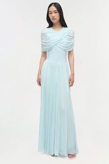 Light blue draped jersey maxi dress with pleated skirt and draped cape overlay across shoulders.