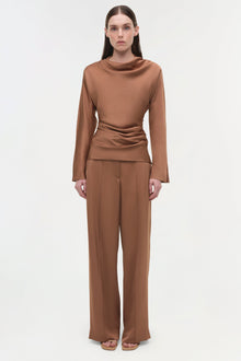 Camel satin long-sleeve top with cowl neckline and ruched side detail, worn with matching wide-leg pants.