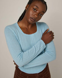 Model wearing Daisy Pointelle Sweater in Light Blue. Daisy Pointelle Sweater is a merino wool long sleeve, square neck, regular fit sweater available in sizes XS-XXL.