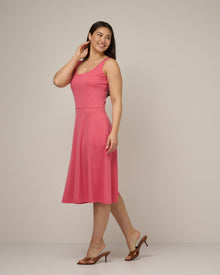 Model wearing Ava Fit & Flare Dress in Geranium, a saturated medium pink color. Ava Fit & Flare Dress is a merino wool sleeveless, scoop neck, midi fit & flare dress with pockets available in sizes XS-XXL.