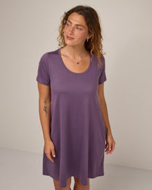Model wearing Maggie Swing Dress in Purple Fig, a soft medium purple color. Maggie Swing Dress is a merino wool short sleeve, scoop neck, knee length swing dress with pockets available in sizes XS-3X Regular, XS-3X Long.