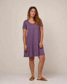 Model wearing Maggie Swing Dress in Purple Fig, a soft medium purple color. Maggie Swing Dress is a merino wool short sleeve, scoop neck, knee length swing dress with pockets available in sizes XS-3X Regular, XS-3X Long.