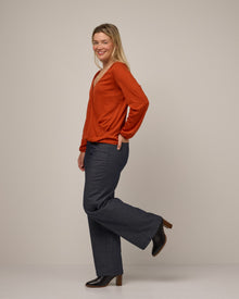 Model wearing Diana Surplice Top in Terracotta, a saturated red-orange color. Diana Surplice Top is a merino wool long sleeve, v-neck, regular fit top available in sizes XS-XXL.