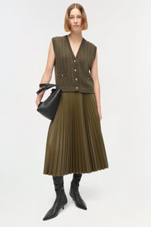 Olive green cable-knit vest with v-neck, button front, and ribbed trim worn over matching pleated skirt.