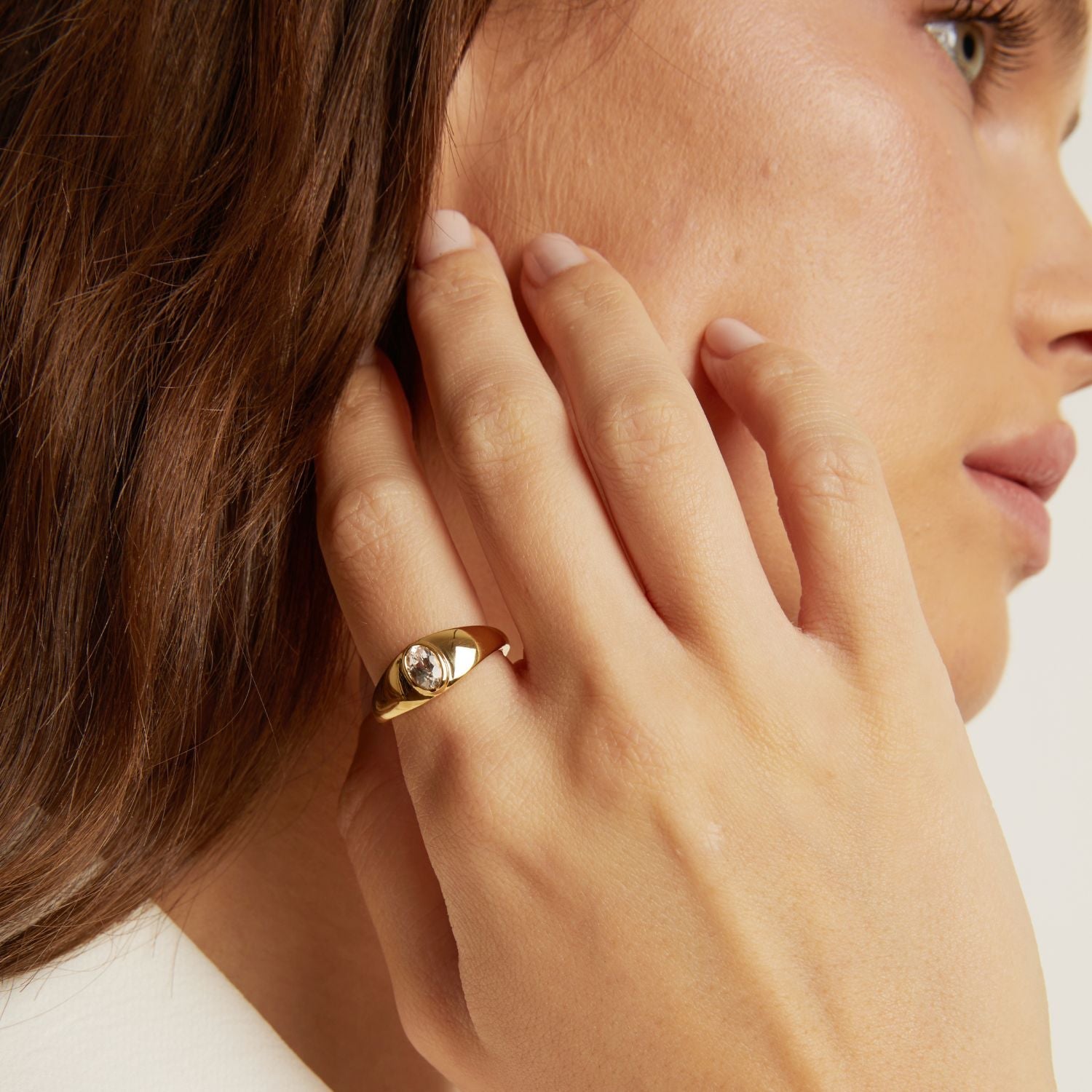 Close-up of a woman wearing a gold ring on her hand, with a neutral background.