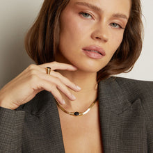 Model. Woman wearing a gold necklace and ring against a neutral background
