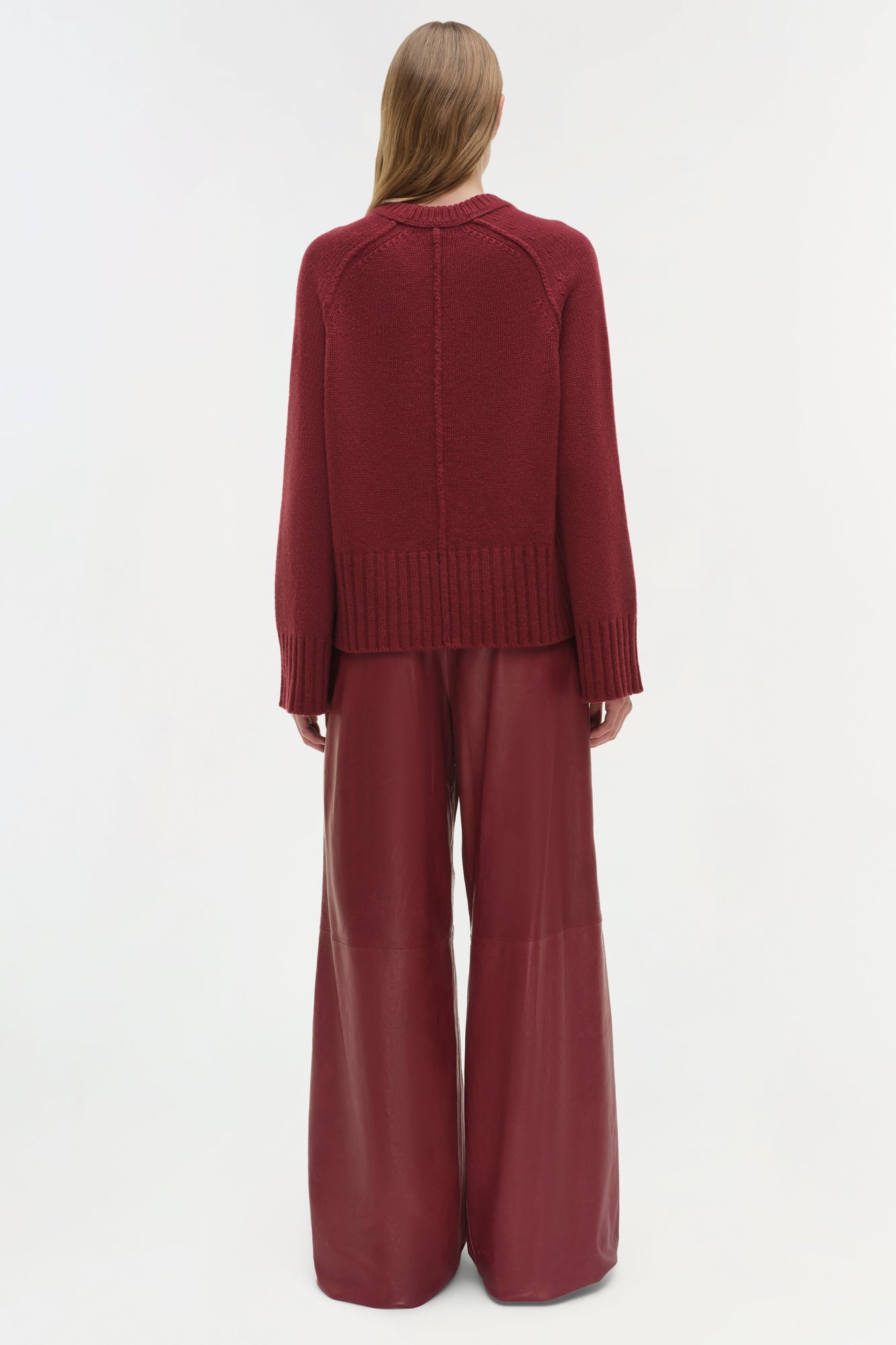 Woman wearing burgundy crewneck cashmere sweater with ribbed cuffs and matching wide-leg pants, shown from back.