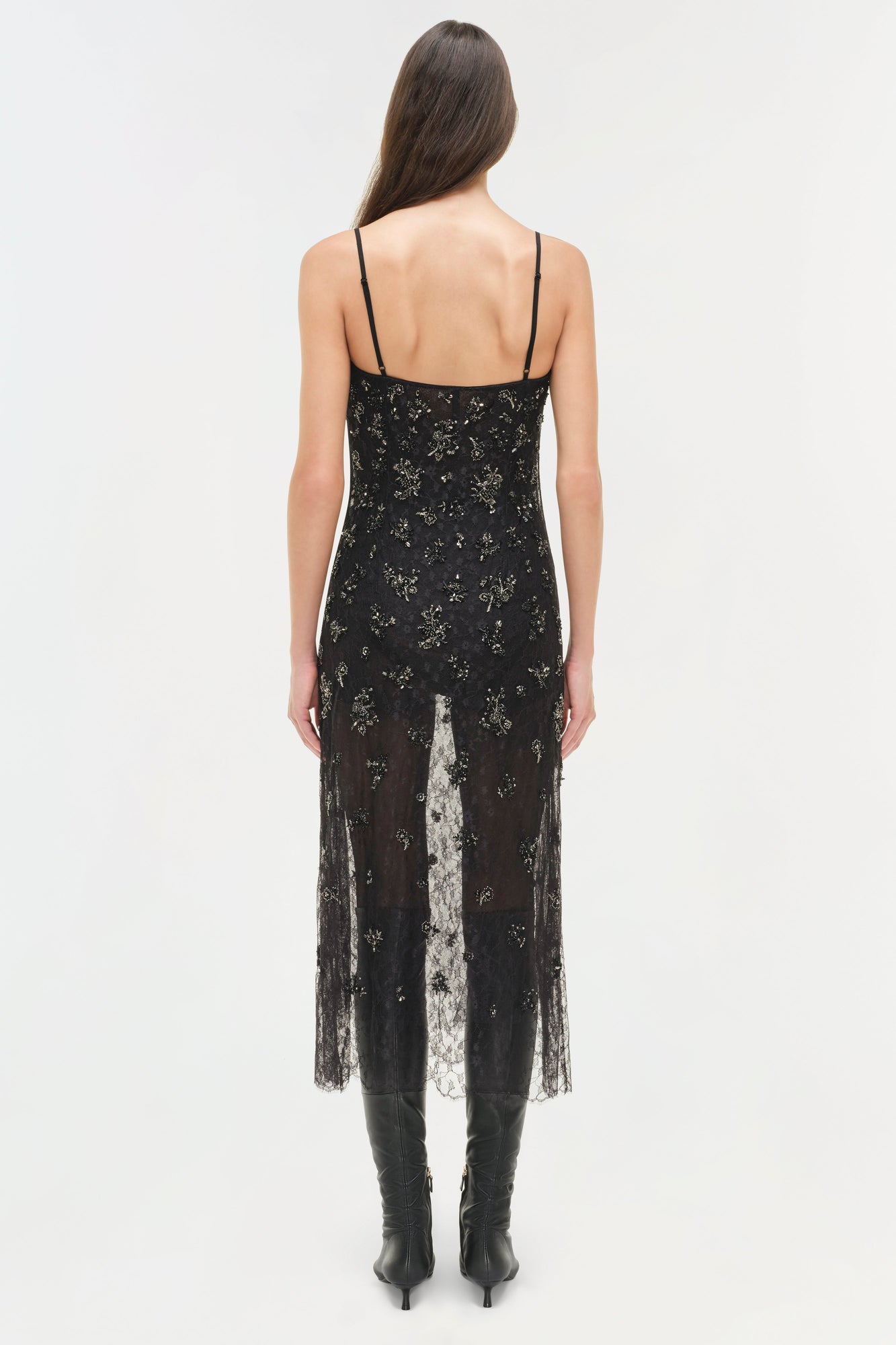 Black lace midi dress with gold embellishments, spaghetti straps, and sheer lace overlay panel, worn with black boots.