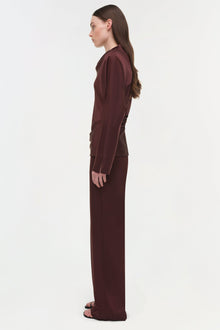 Burgundy satin long-sleeve top with draped fabric detail, shown on model in side profile.