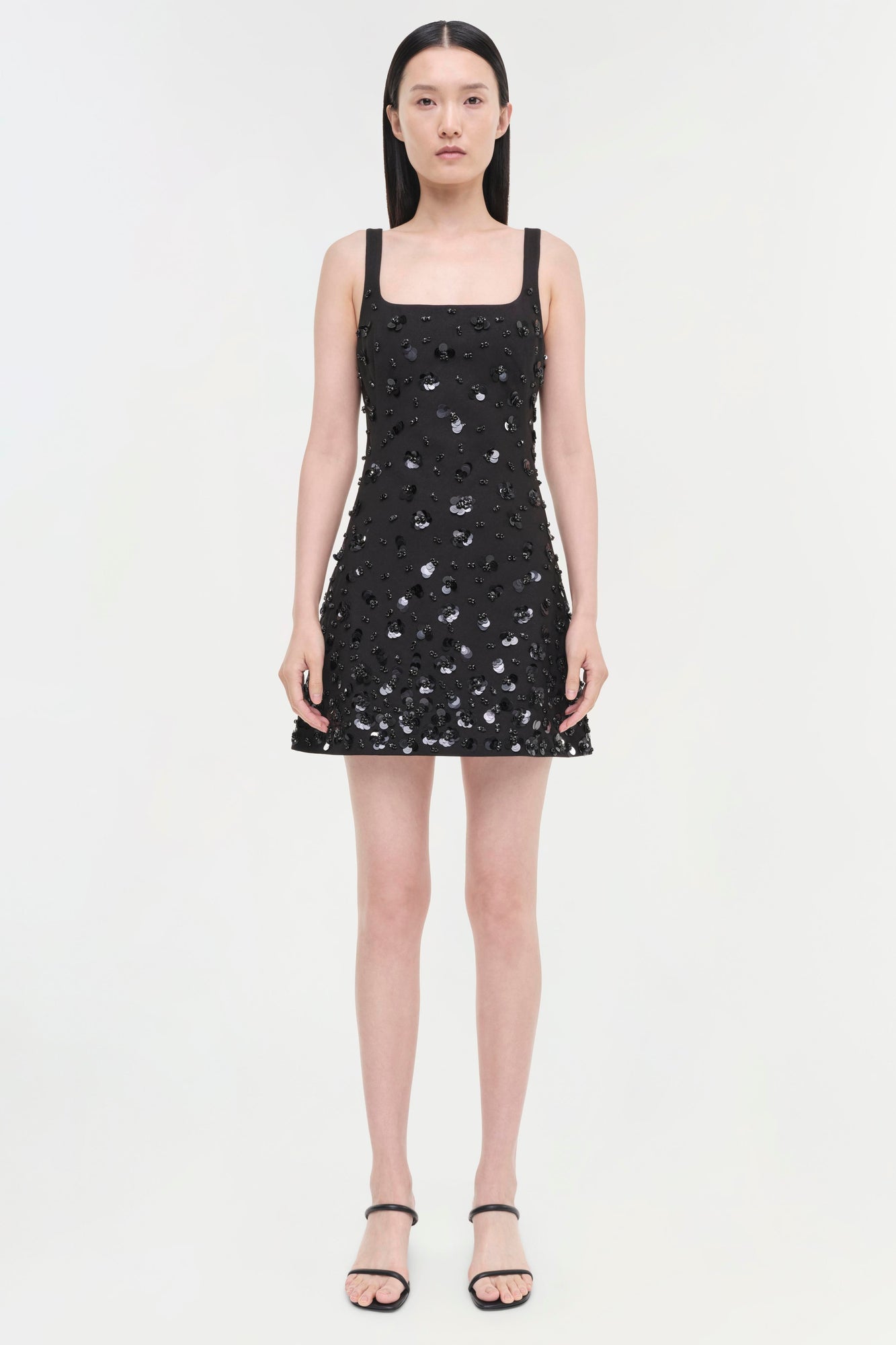 Black sleeveless dress with silver sequin embellishments and a square neckline, displayed on a model wearing black sandals.