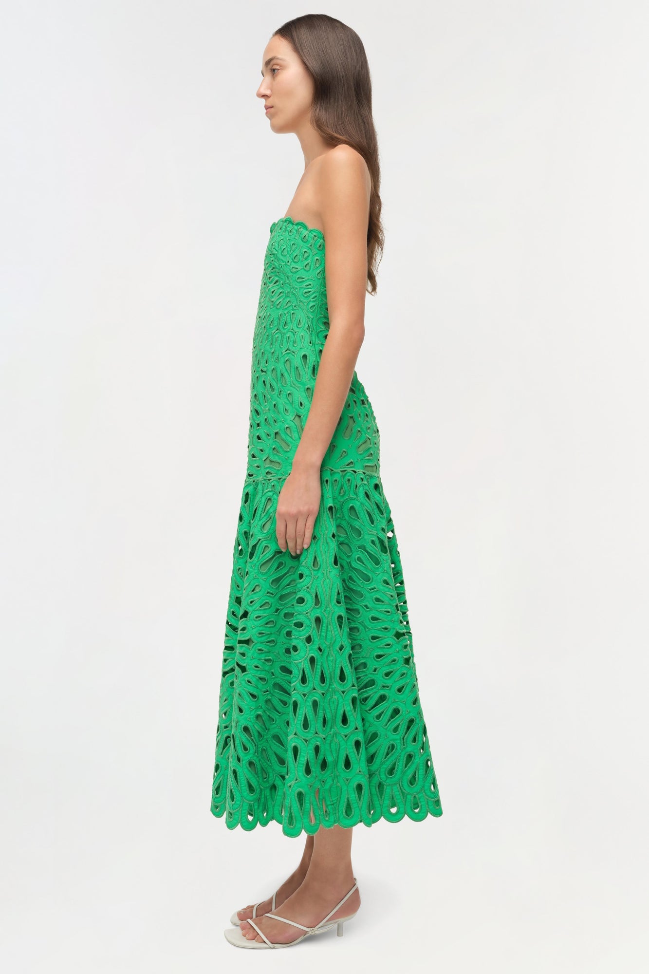 Green strapless midi dress with cutout embroidered pattern, modeled on woman in side profile.