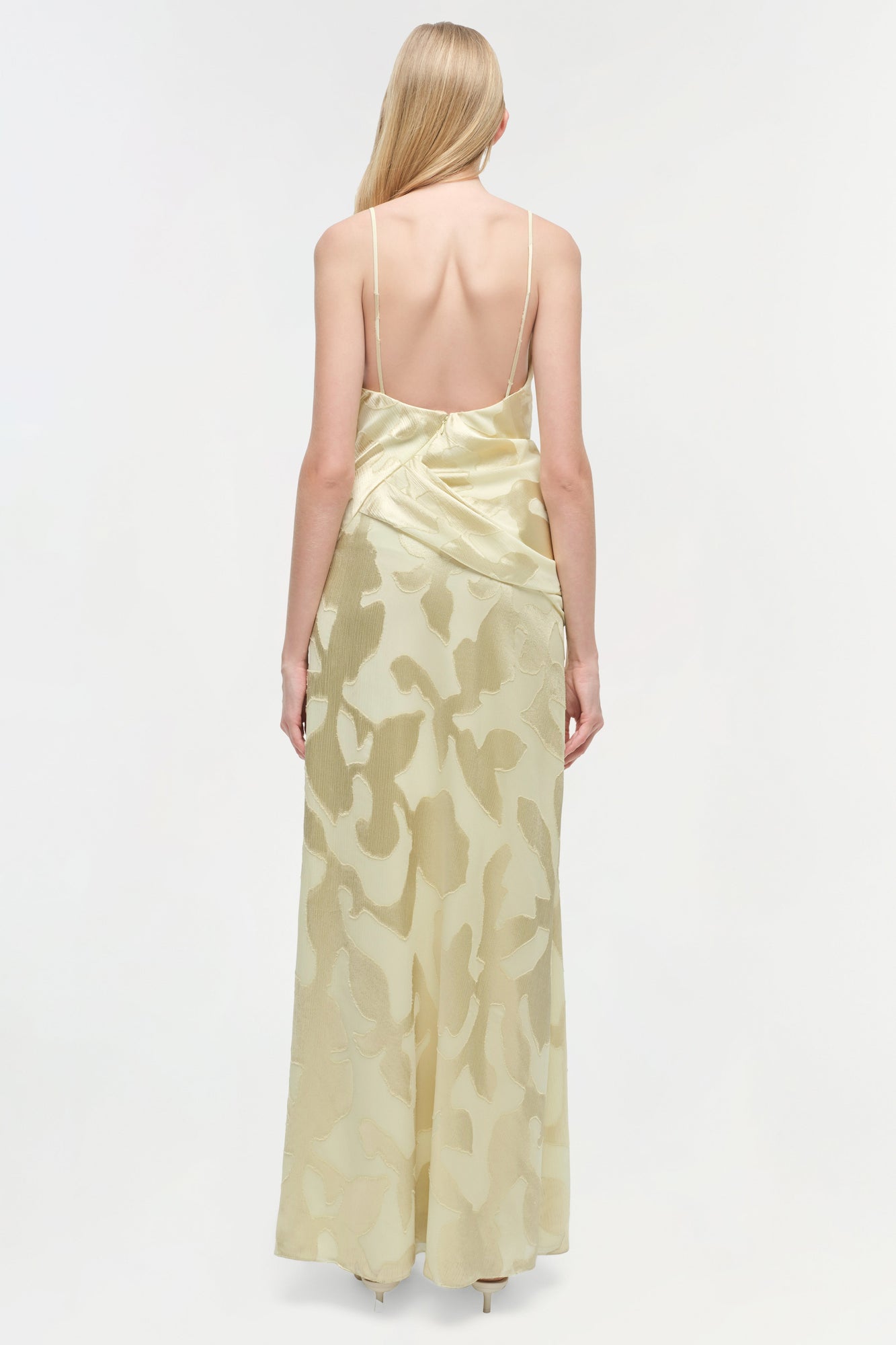 Cream-colored floor-length gown with abstract pattern, thin straps, and open back shown from behind on model.