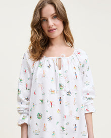 The Women's Twill Delphine Nightgown in 12 Days of Christmas is a white, long-sleeve nightgown with a gathered neckline, small bow tie, and a festive print inspired by the 12 Days of Christmas.