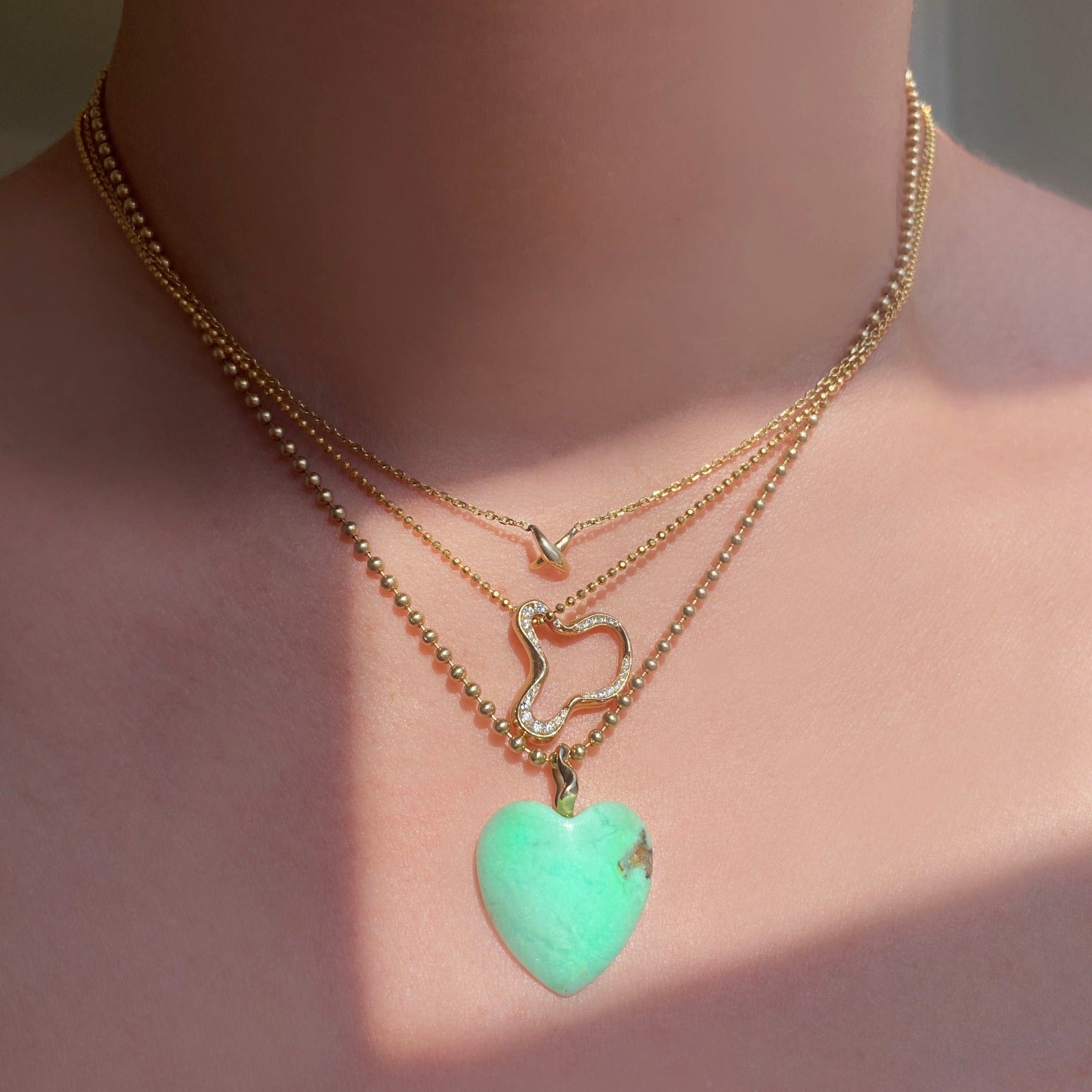 14k gold Demi Pavé Ripple Charm. Styled on a neck hanging from a diamond cut bead necklace layered with multiple chains and charms