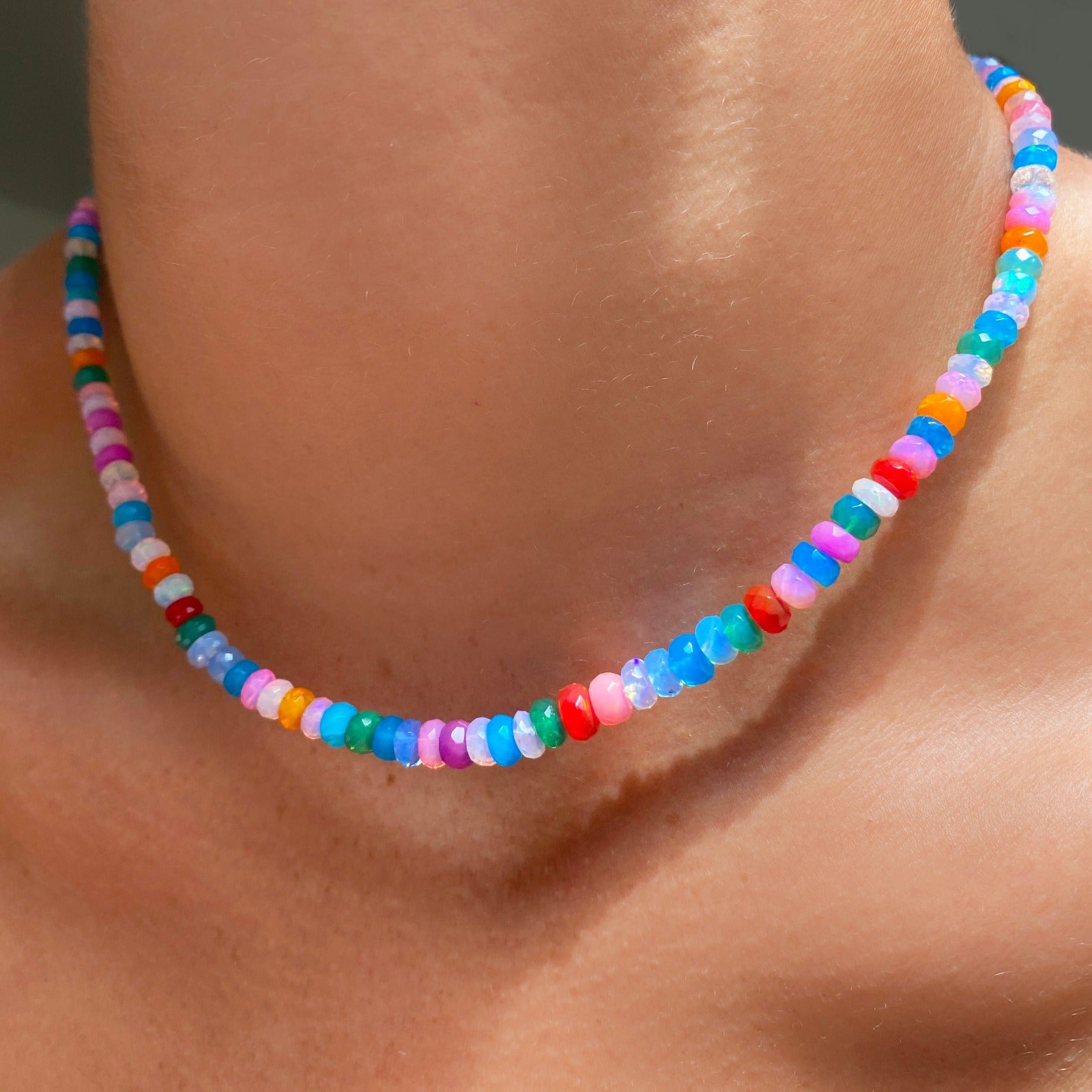 Shimmering beaded necklace made of faceted opals in shades of fiery blues, yellows, red, teal, and purple on a gold linking ovals clasp. 