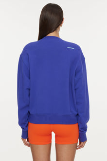 Model wears a royal blue crewneck sweatshirt with the lettering 