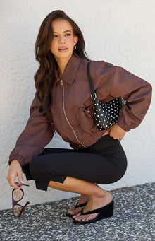 Side view of a chocolate brown cropped bomber jacket with drawstring front pockets and elasticated cuffs