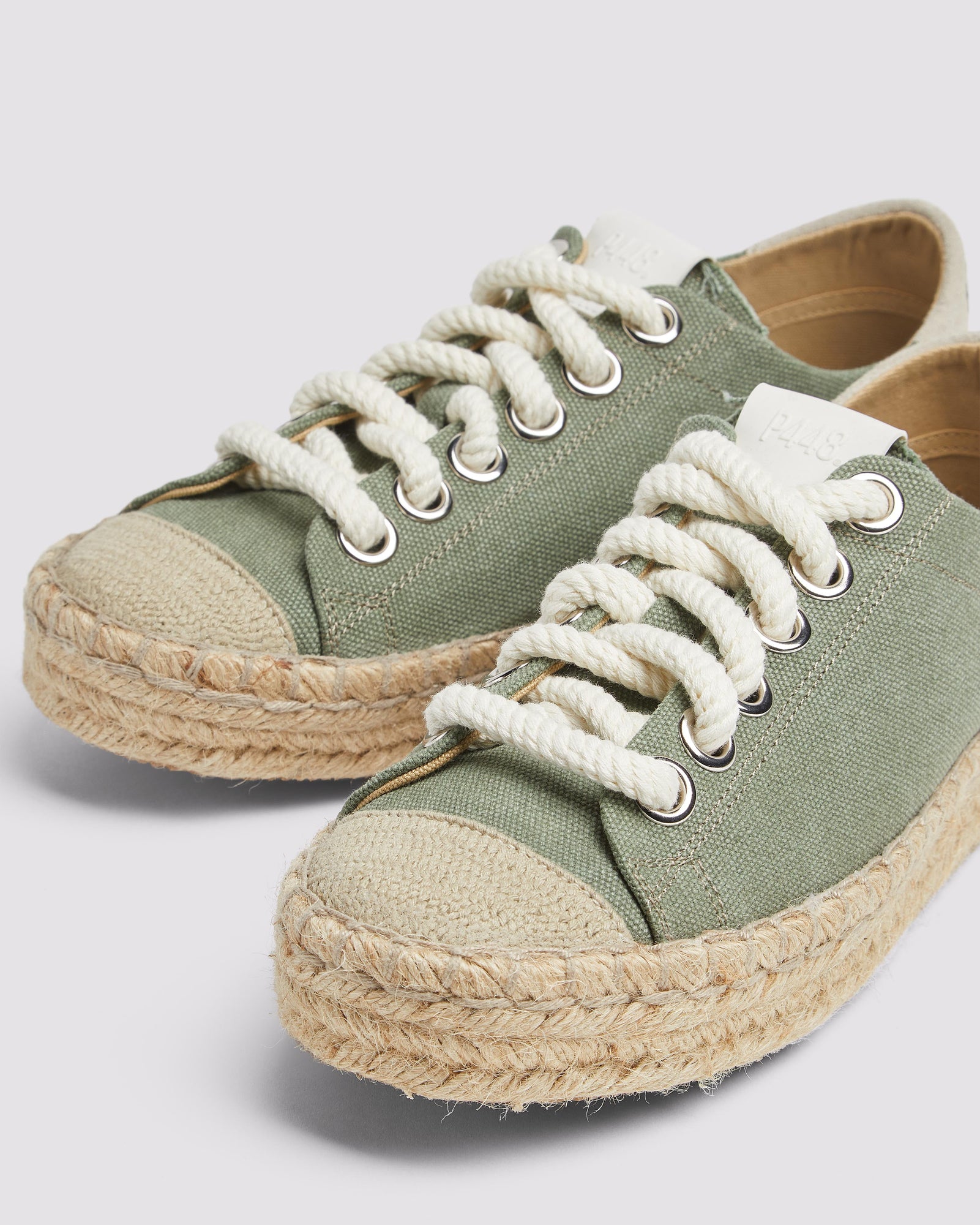 Close-up of P448 green canvas low-top sneaker featuring tan recycled suede heel tab, white rope laces, and organic jute sole for a sustainable style.