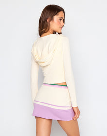 Woman wearing a cream-colored long-sleeve top and a purple skirt with a white background