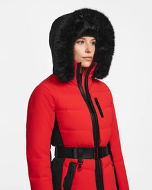 Wearing the Rudsak ALAIA - 8124816 Flame Red, a red and black belted winter coat with black faux fur trim, a person looks slightly to the side against a plain white background.