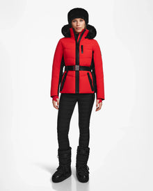 A woman models the Rudsak ALAIA - 8124816 Flame Red quilted ski jacket with black pants, winter boots, and a fur hat, standing facing forward against a plain white background.