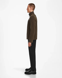 A man stands in profile facing left, wearing the Rudsak ARAGON - 6524539 Army mens fleece full-zip jacket with vegan leather trims, black pants, and black boots against a plain white background.