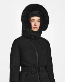 A woman wears the Rudsak CHRISTEL M-M - L124505 Black down puffer coat with a belted waist and fur-trimmed hood, facing forward against a plain white background.