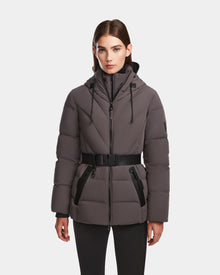 A woman wears the Rudsak ENZAH - 8124692 grey belted, hooded mid-length quilted puffer coat with black zippers and drawstrings, standing against a plain white background.