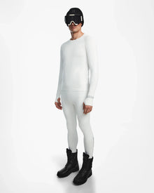 A person wearing the Rudsak FRANC - 6524541 Iceland white stretch base layer top and matching leggings, paired with black winter boots, a black beanie, and ski goggles, stands against a plain white background.
