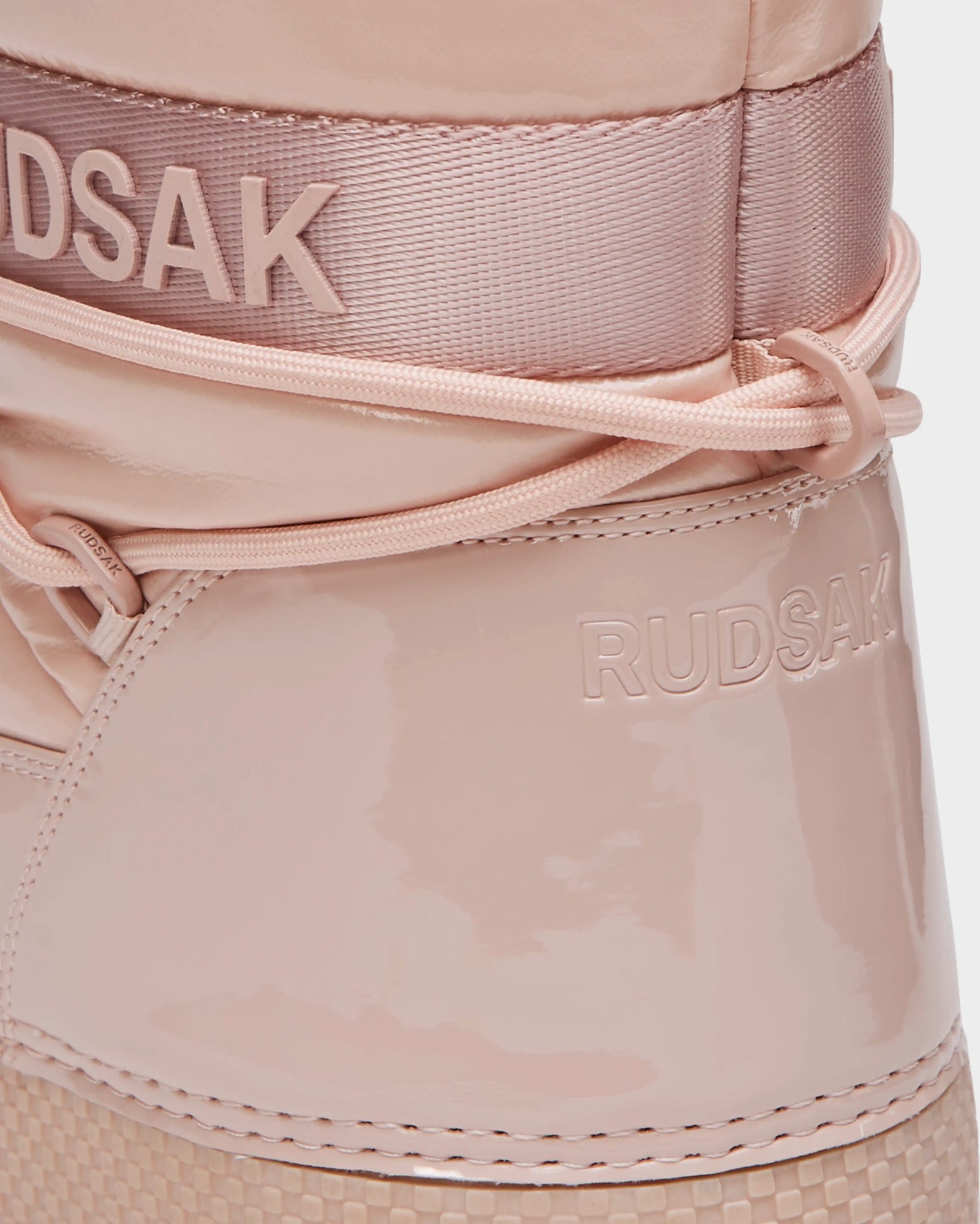 Close-up of the HARLOW Y - 1223500 kids’ winter boot by Rudsak, in pastel pink with RUDSAK branding on upper fabric and lower leather, decorative laces, and a textured sole.