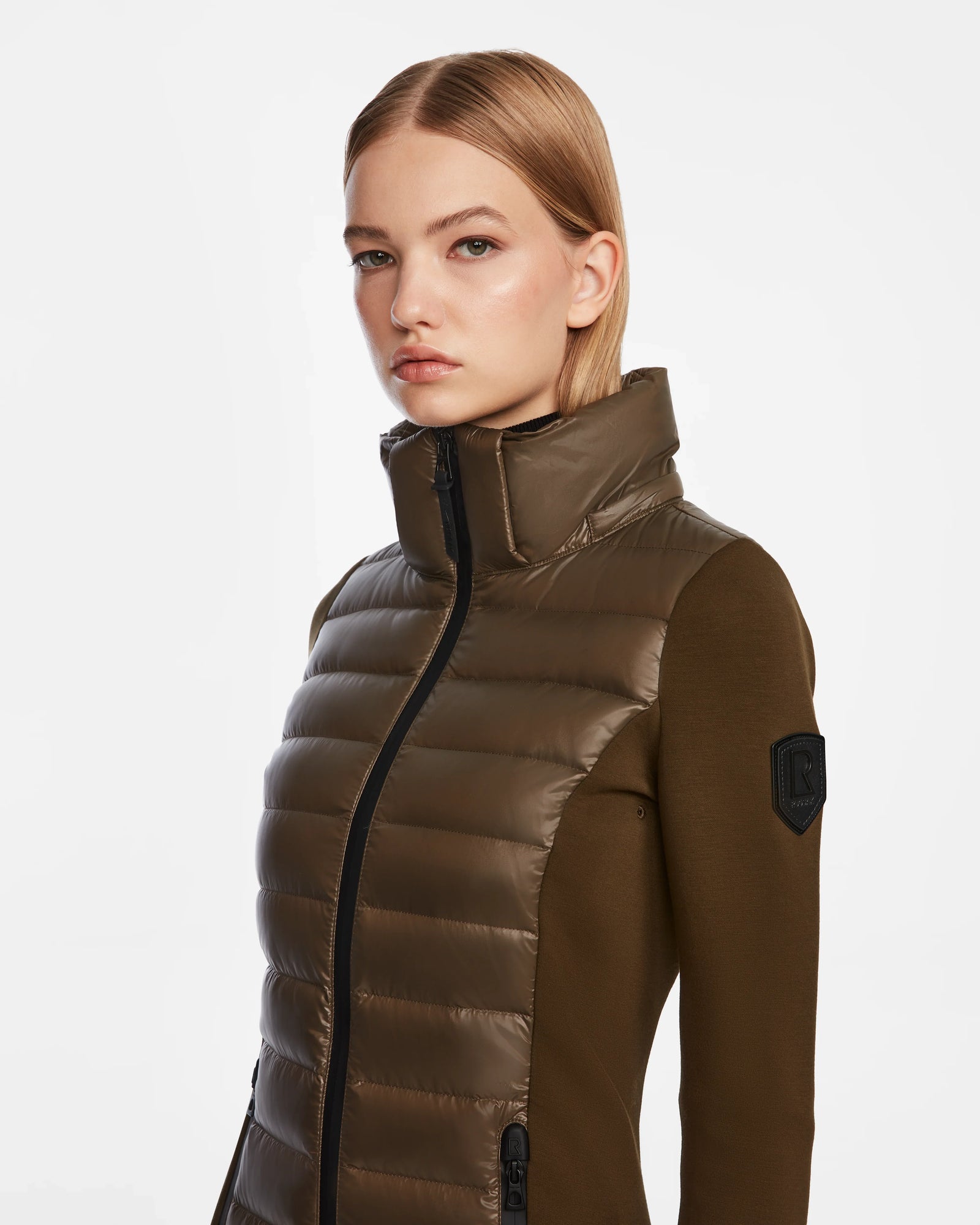 A woman with straight blonde hair wears the Rudsak MARRY - L121003 Light Olive women’s puffer jacket with a high collar and black zipper, standing against a plain white background.