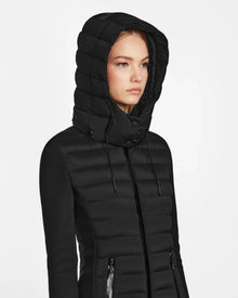A young woman models the RUDSAK MERINA - 8122546 BLACK, a black hooded quilted down jacket with zippered pockets, perfect for everyday style—shown against a plain white background.