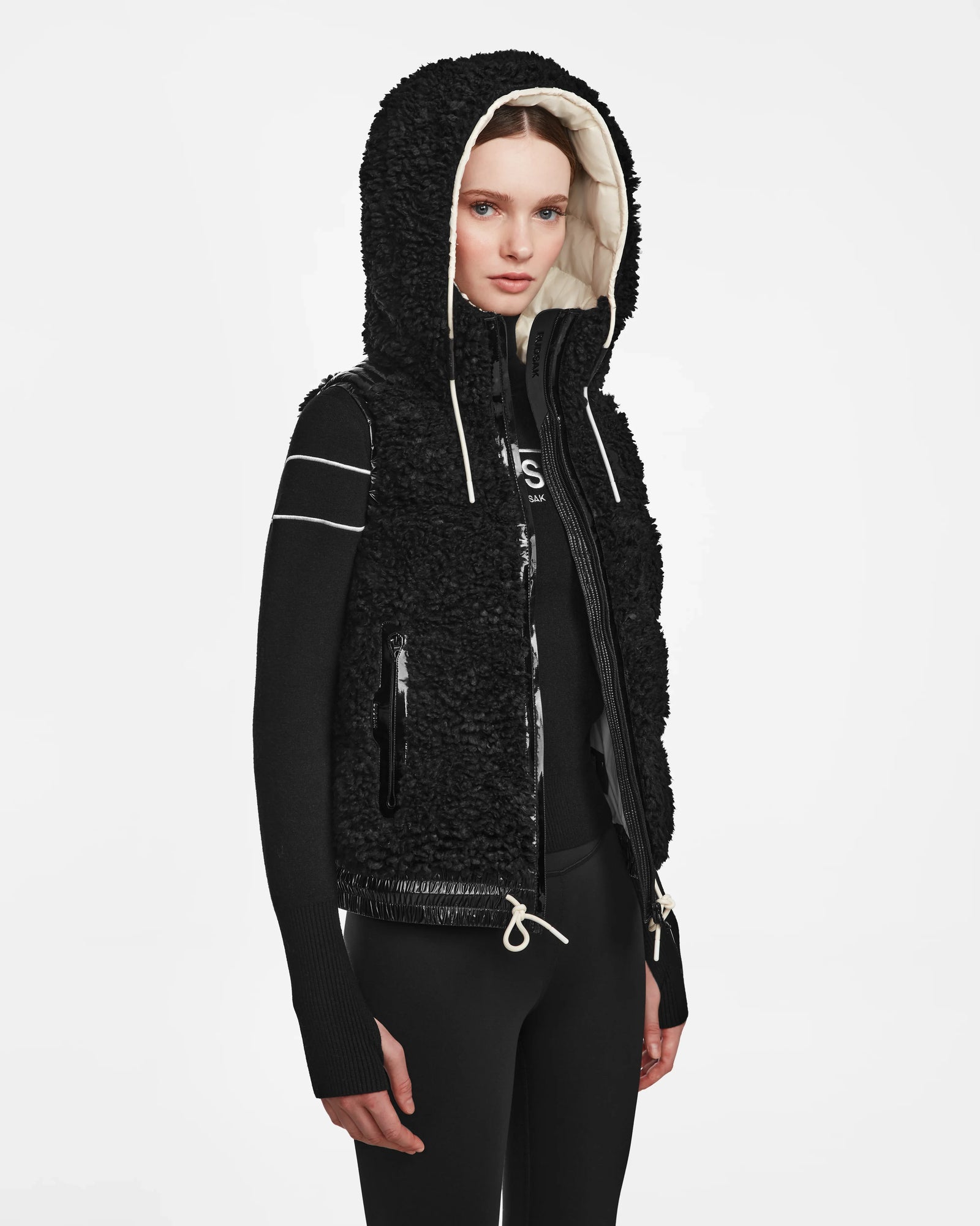 A woman models the Rudsak RAQUEL S - 8124526 Black teddy ski vest over a black long-sleeve top and black pants, standing against a plain white background, ready for winter adventures.