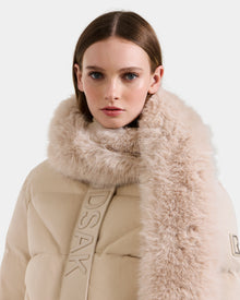 A woman with straight brown hair wears the Rudsak CARMY - L425534 Vanilla puffer coat with a plush fur collar, standing with a serious expression against a plain light background.