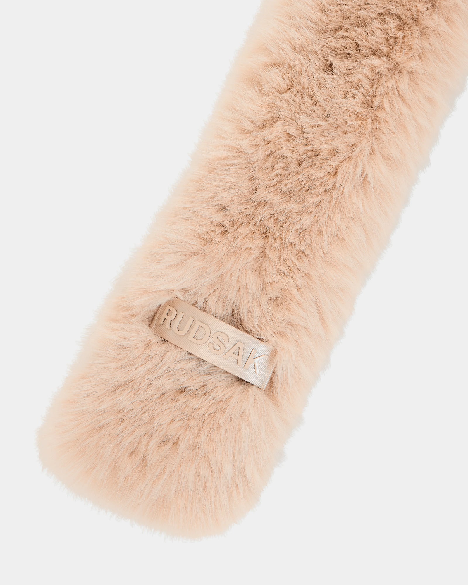 Close-up of the CARMY - L425534 Vanilla, a soft, light beige women’s faux-fur scarf by Rudsak, featuring a rectangular leather patch embossed with the brand name—offering plush warmth and stylish cold-weather comfort.