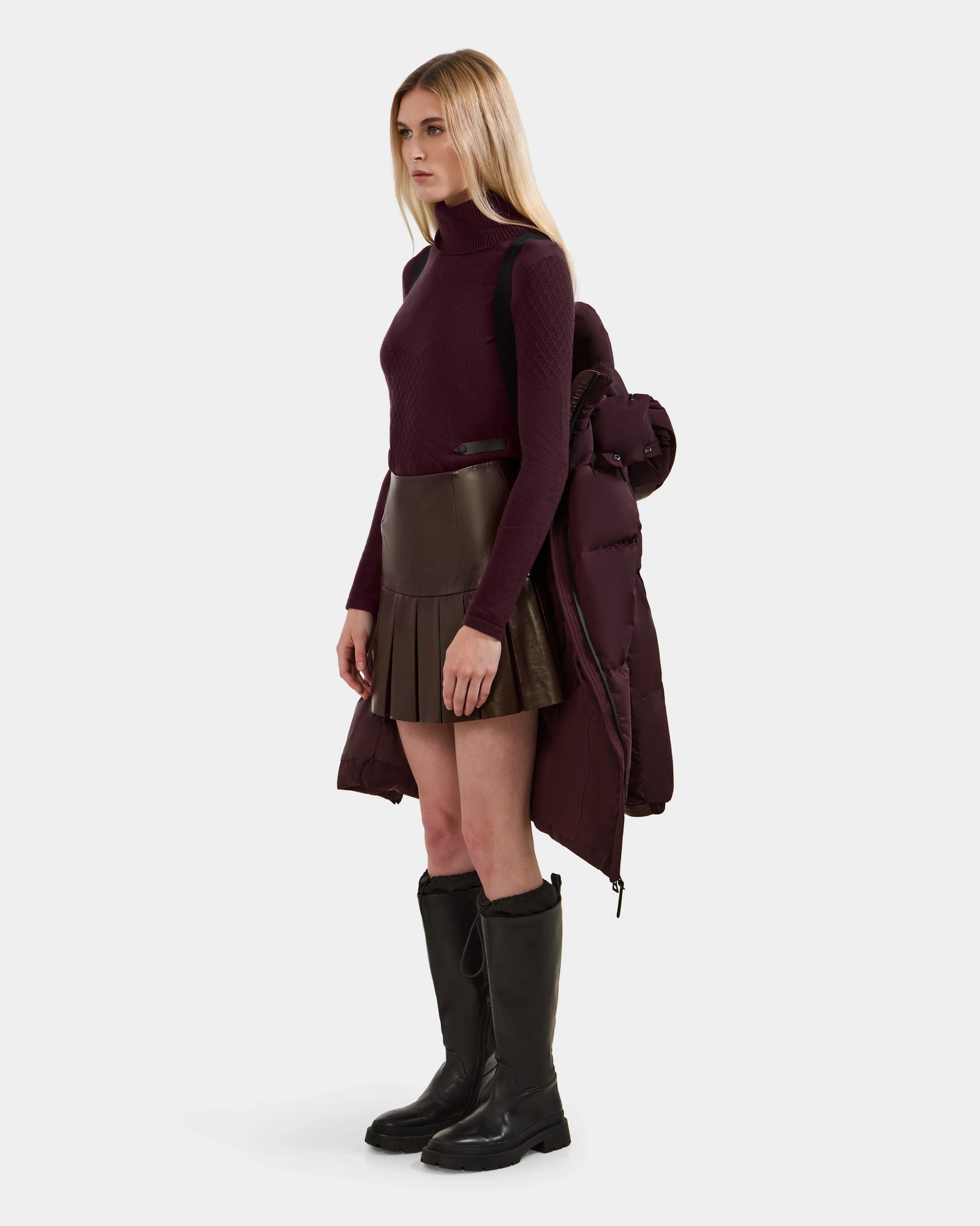 A woman with long blonde hair poses against a plain background, wearing Rudsak's KARLEE L - 8125682 Bordeaux women's long down puffer coat draped over her shoulders for stylish, cold-weather wear.