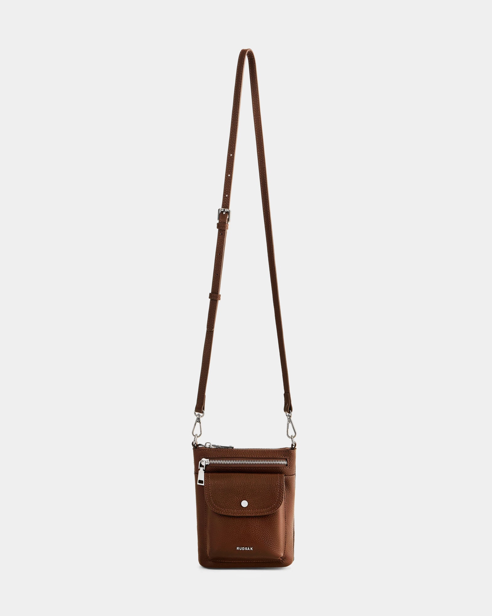 The Rudsak LILA - L325513 Mocha is a women’s crossbody bag in pebbled leather, featuring an adjustable strap, front flap pocket with snap closure, zippered main compartment, and a subtle embossed brand name at the bottom.