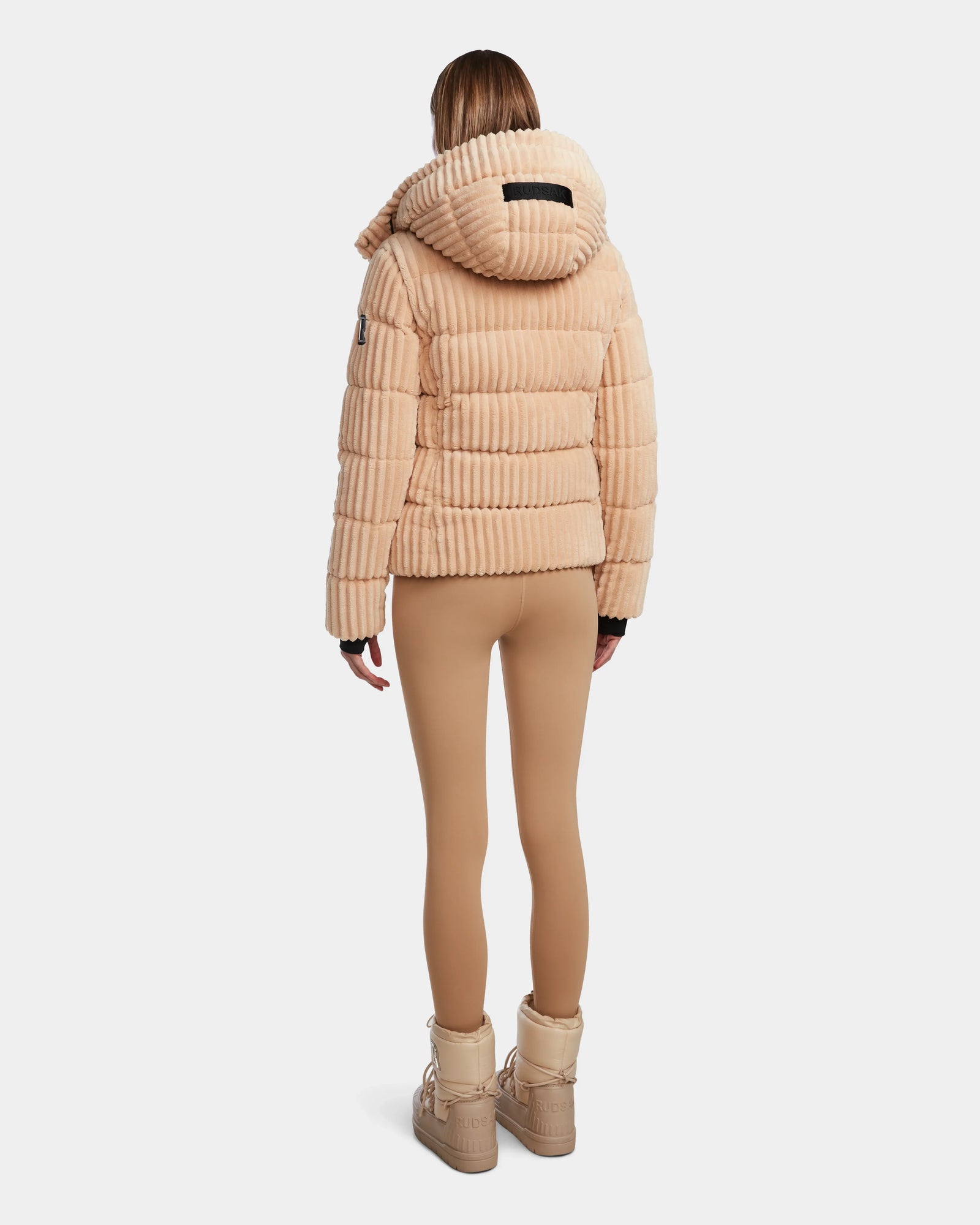 A person faces away, wearing the MIRRY FF - L124507 Iceland beige velvet corduroy puffer with hood by Rudsak, tan leggings, and beige boots against a plain white background.