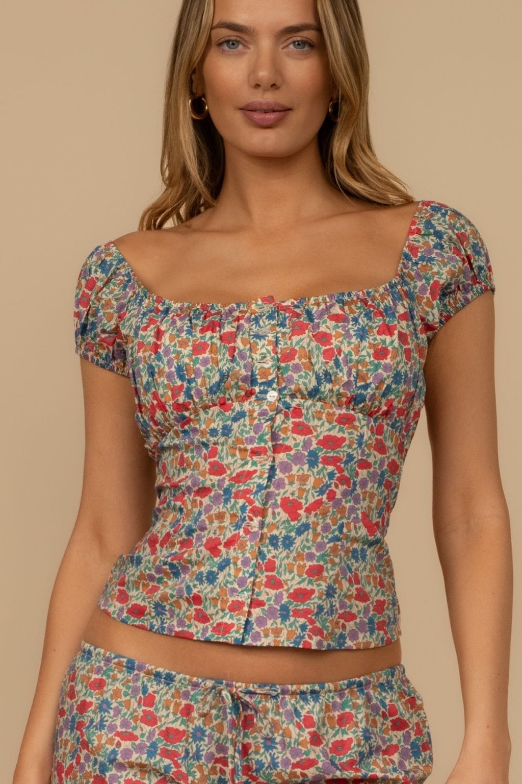 Woman wearing multicolored floral print top with short puffed sleeves and scoop neckline.