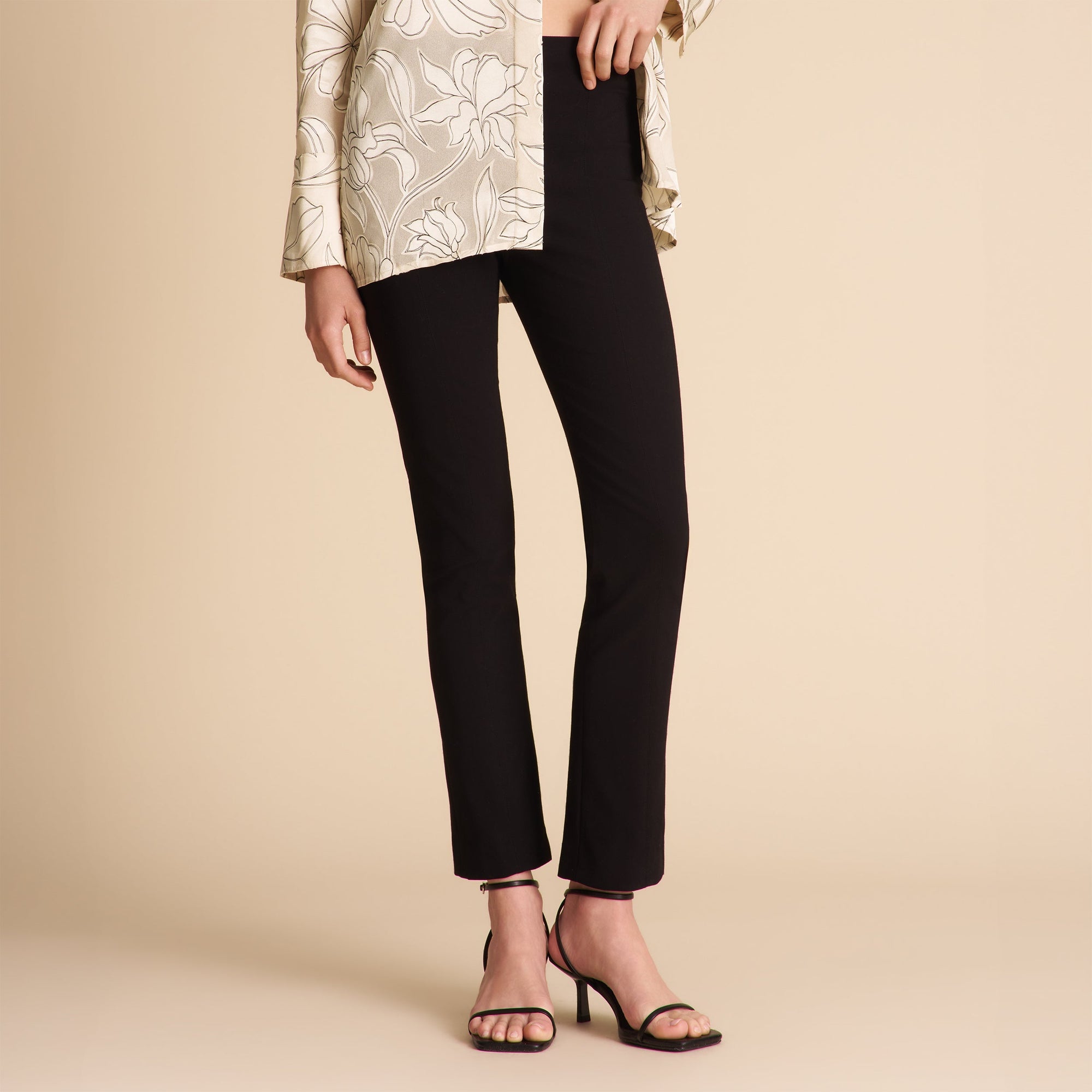 Person wearing black pants and a patterned top on a beige background | Exclude