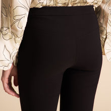 Person wearing black pants and a patterned top on a beige background