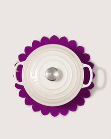 A white Le Creuset dutch oven with handles rests on a graf lantz trivet inspired by Japanese floral crests, providing stylish heat protection in the kitchen against a light background.