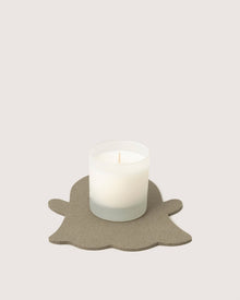 A white candle in a frosted glass holder by Graf Lantz rests on a gray, ghost-shaped coaster against a plain, light background.