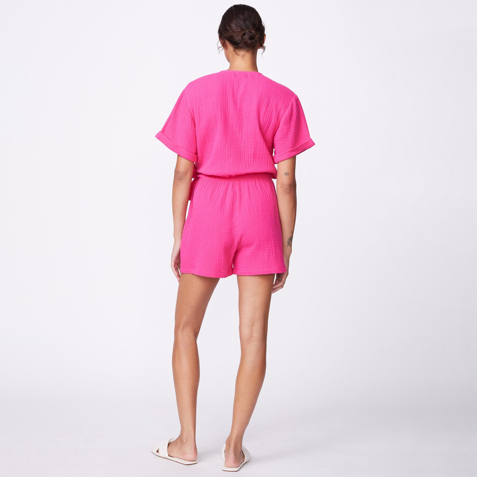 Back view of model wearing the gauze wrap romper in raspberry.