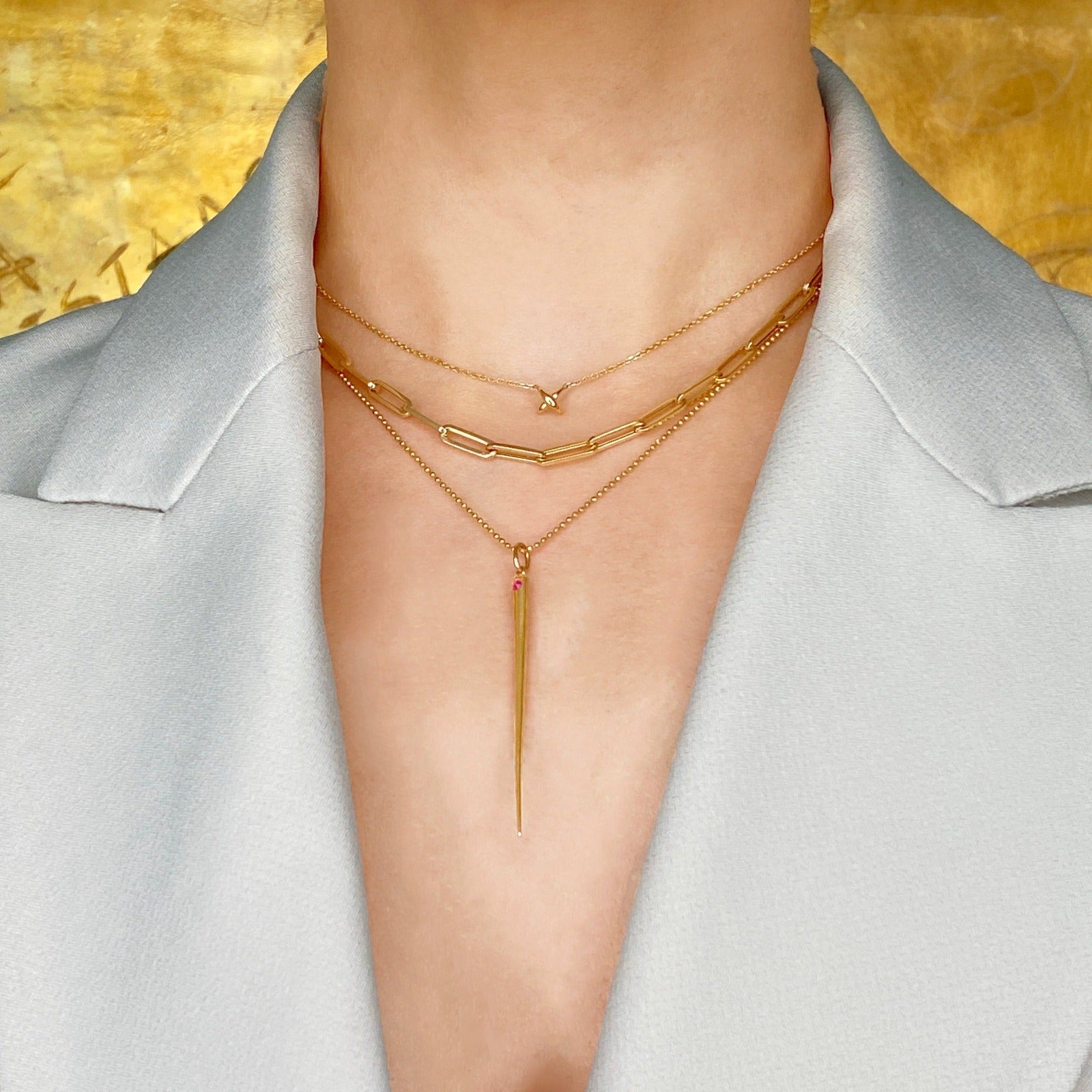 14k gold Stitch Necklace styled on a neck layered with the chunky paperclip chain necklace and diamond cut bead chain with Quill Spike charm with ruby accent attached. 